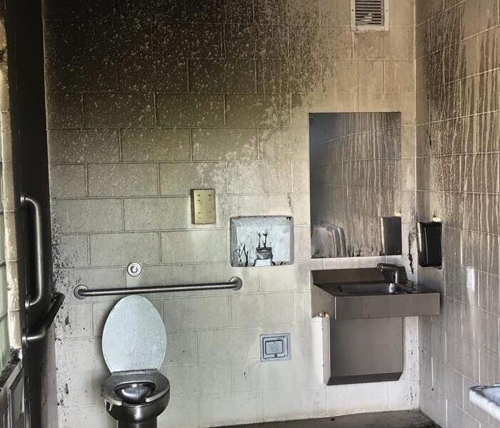 Public restroom with silver toilet covered in black soot. 